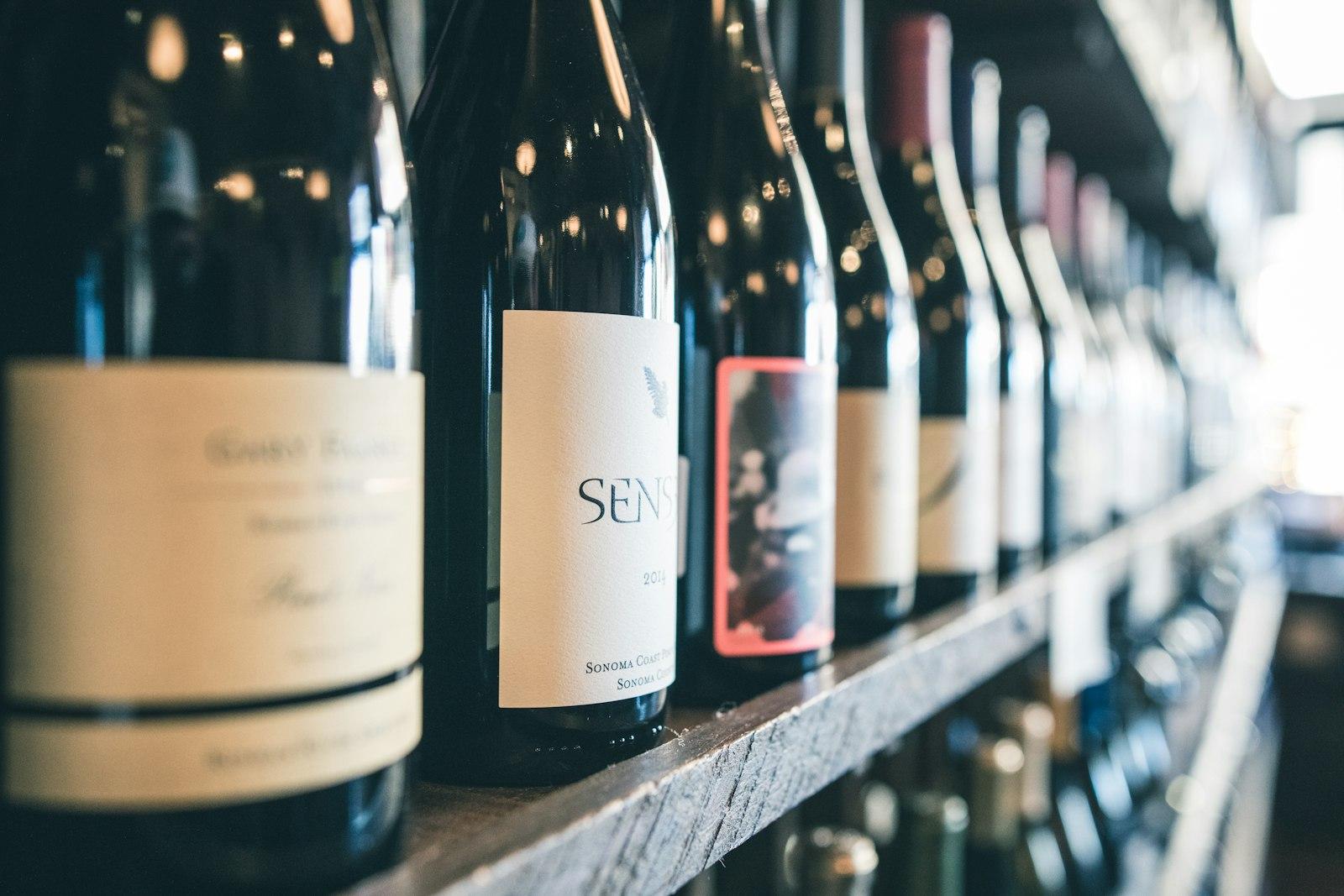 Row of wine bottles standing on a wooden shop shelf