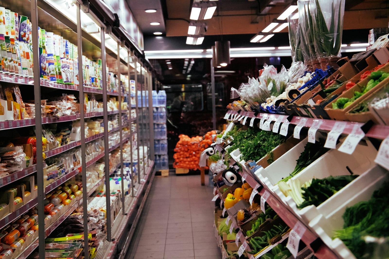 Narrow aisle in a small grocery shop with chiller cabinets and fresh produce