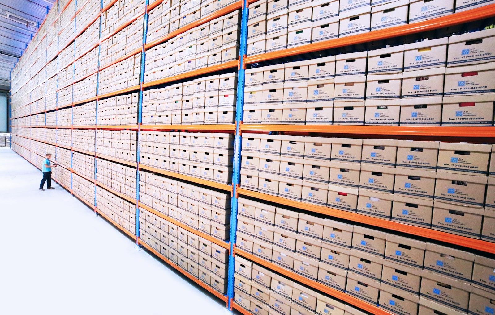 Stocktaker beside tall racking stacked with labelled cartons